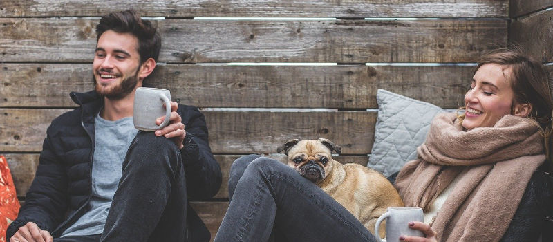 man and woman with mugs and pug in lap
