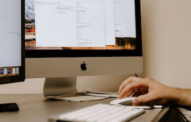 Person uses mouse while working on a Mac desktop computer