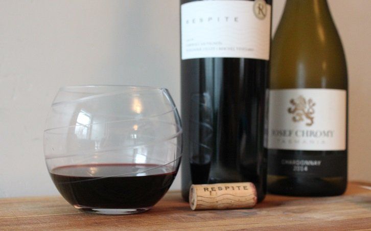 A nearly empty glass of wine next to two bottles of wine