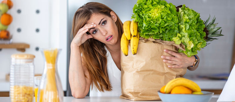frustrated or tired woman holding grocery bag filled with bananas and greens