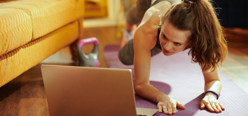 Woman works out on yoga mat in front of a computer