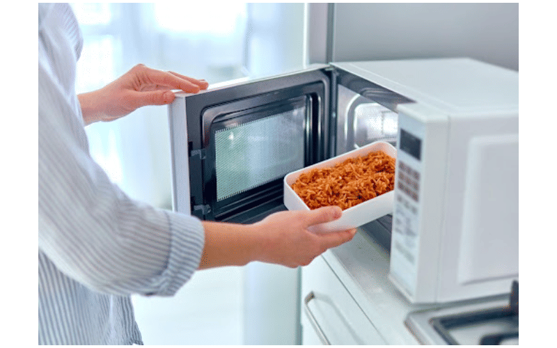 person putting pasta dish into microwave