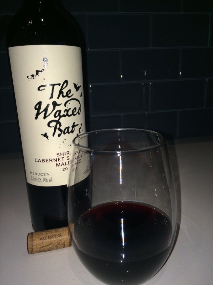 A bottle of The Waxed Bat wine next to a half-filled wine glass