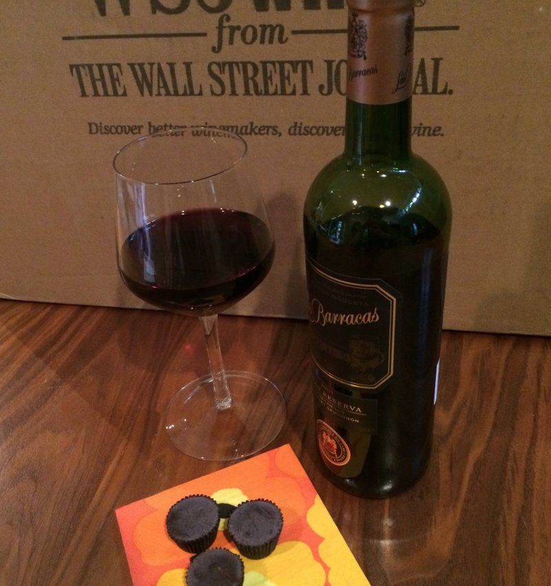 An opened bottle of Barracas wine next to a half-filled wine glass and chocolates