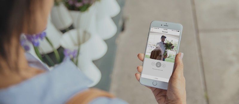 Woman holding phone with doorbell security footage showing delivery man ringing doorbell