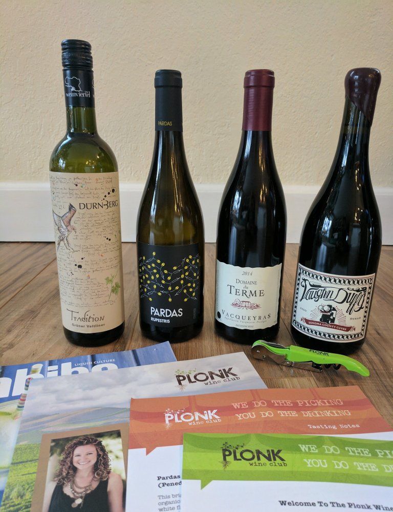 Four wine bottles in front of the Plonk wine newsletter and wine cards