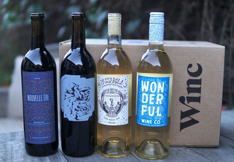 A line-up of four wine bottles in front of a cardboard box that has the Winc logo on it