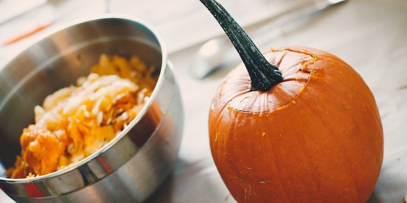 A pumpkin sitting next to a bowl of pumpkin seeds
