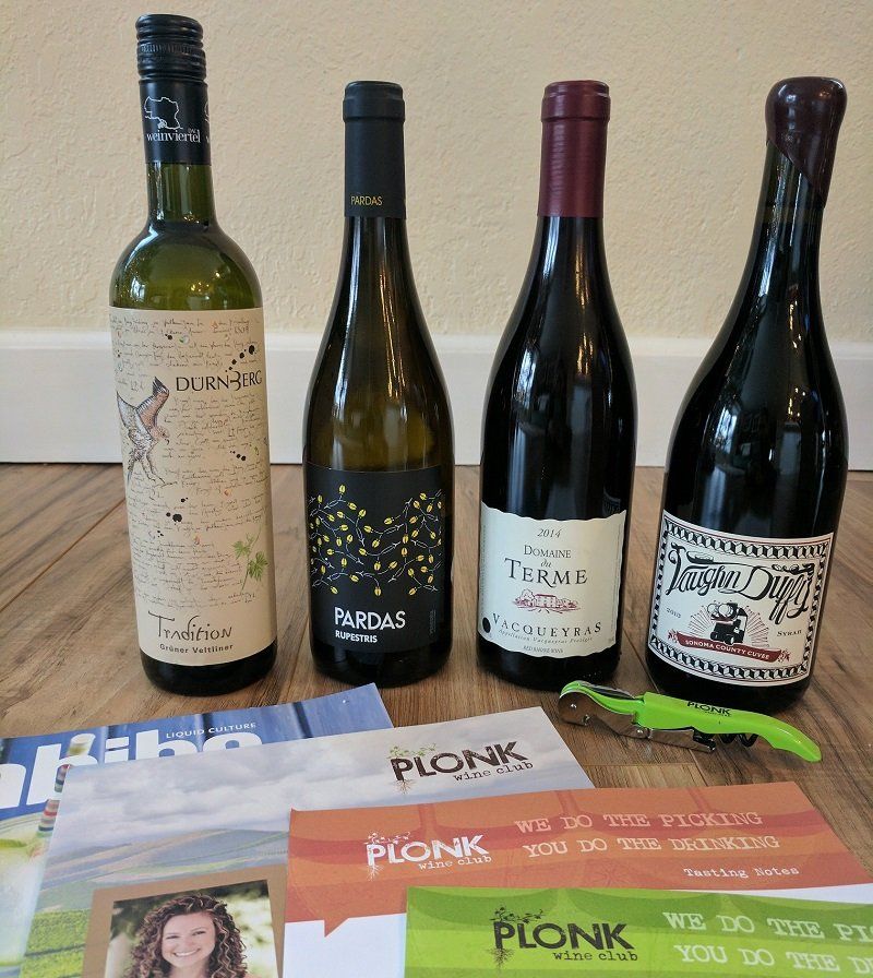 Four bottles of wine in front of Plonk Wine Club newsletters