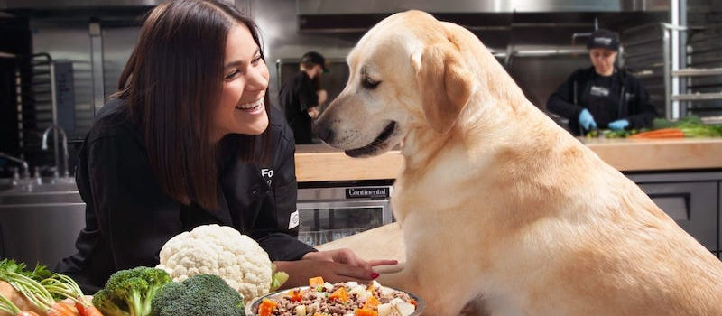 Woman and yellow lab stand in kitchen near fresh produce and recipe